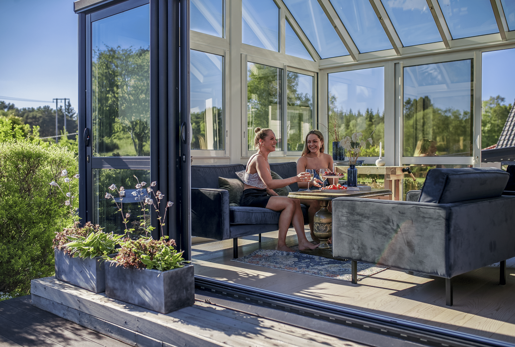 To kvinner som sitter i en sofa og drikker, inne i en Veranda vinterhage.